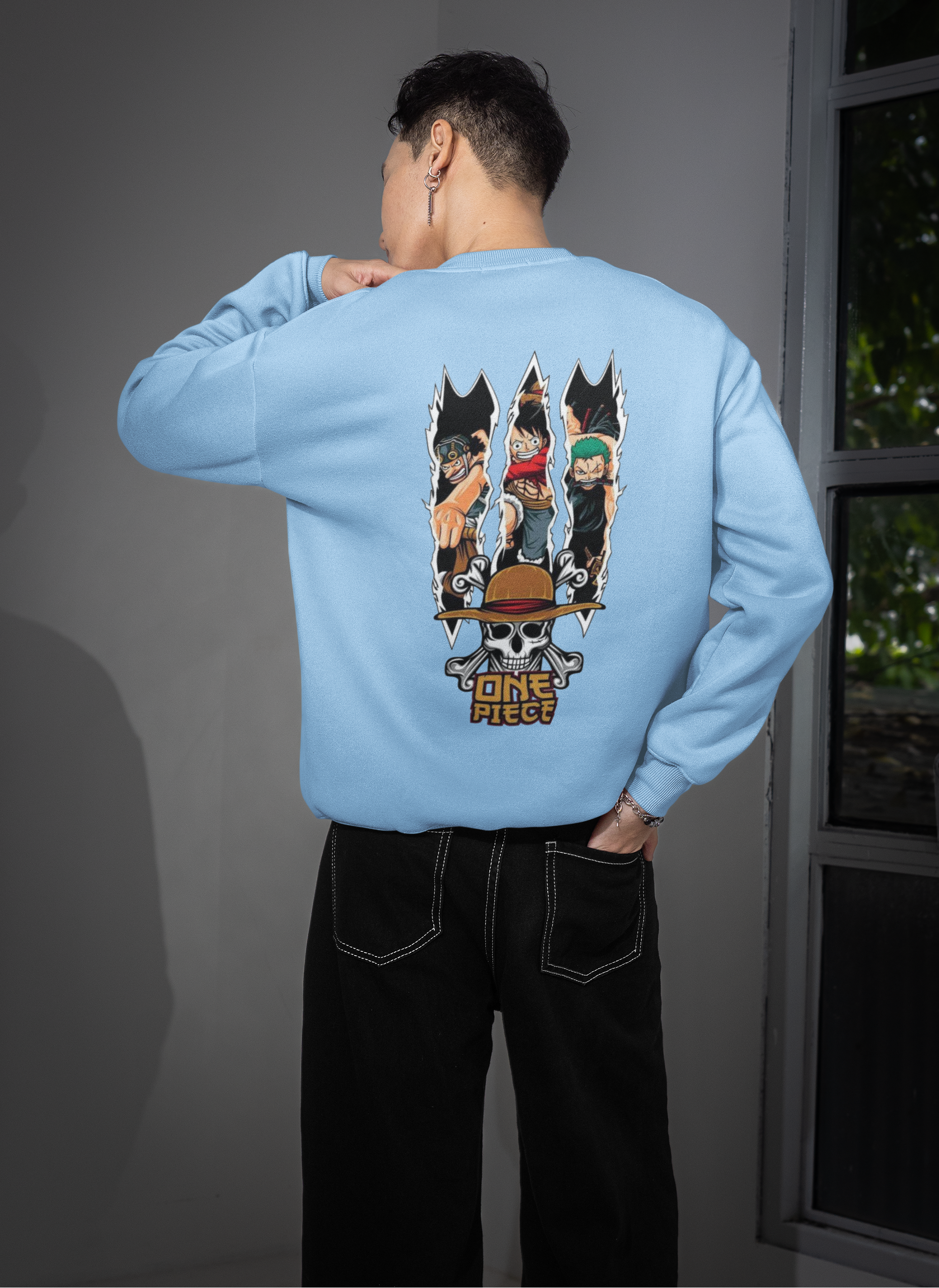 Person wearing a light blue sweatshirt with 'One Piece' character designs on the back, standing indoors.
